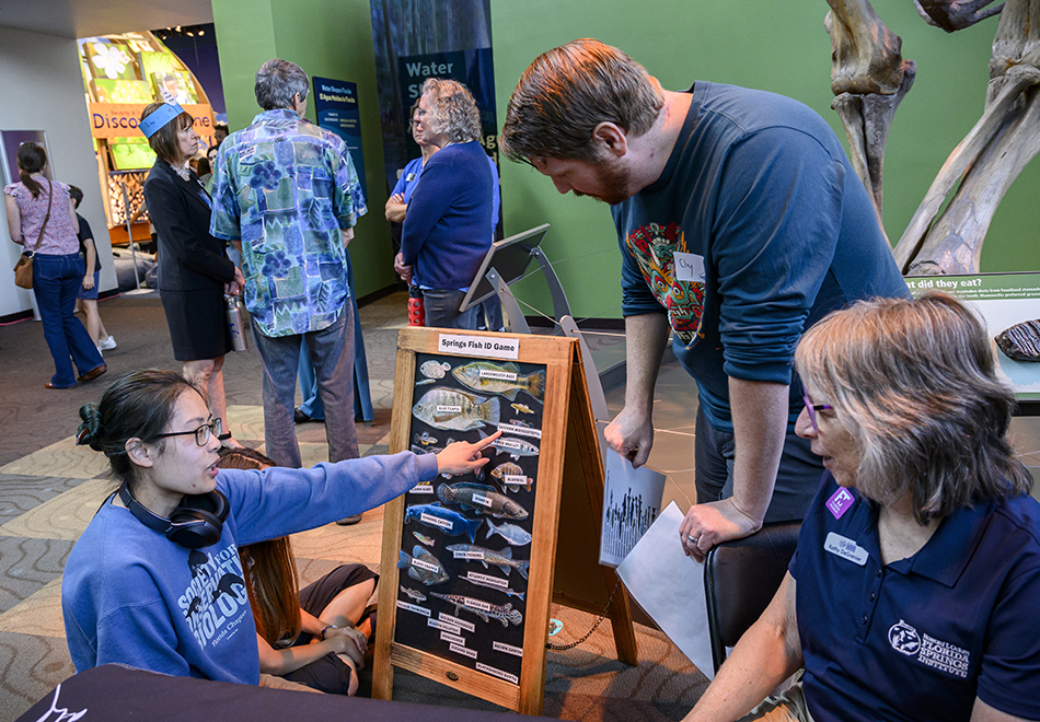 a person is kneeling and pointing at fish stickers on a board to 2 people