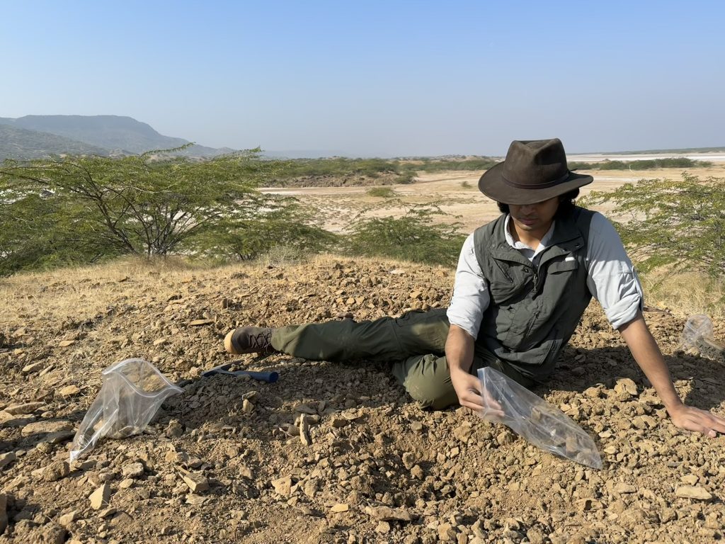 Person puts fossils into a plastic bag while working outside in an arid region.