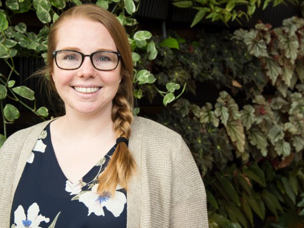 Person smiles in front of green plants.