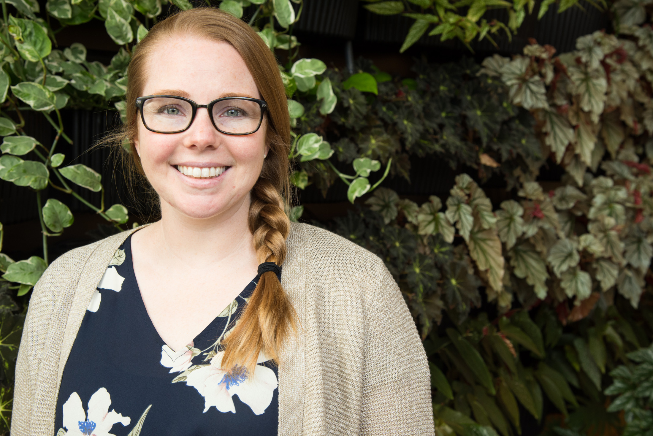 Person smiles in front of green plants.