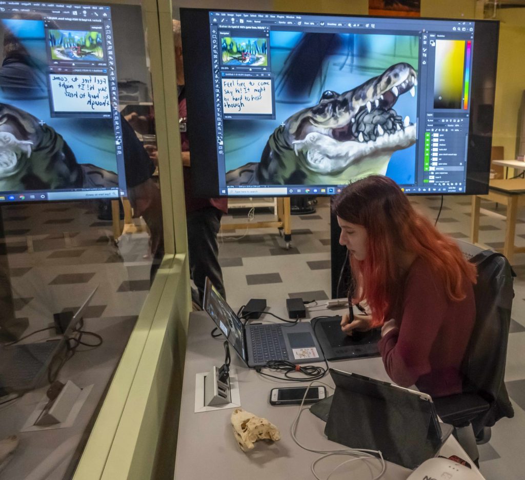 Person uses a stylus to digitally illustrate an alligator in a museum exhibit.