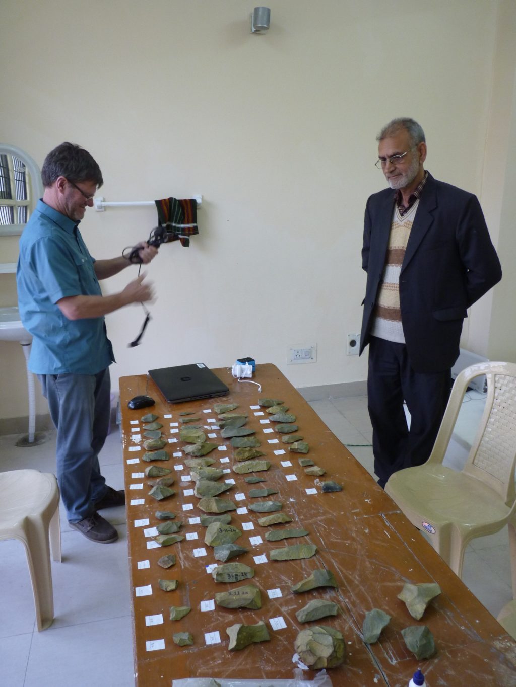 Two scientists stand over a long table with several stone tools laid out