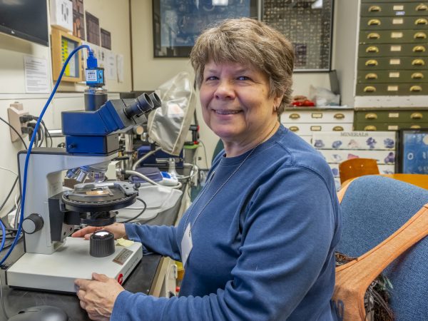 Person sitting in front of a microscope and smiling for the camera.