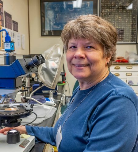 Person sitting in front of a microscope and smiling for the camera.