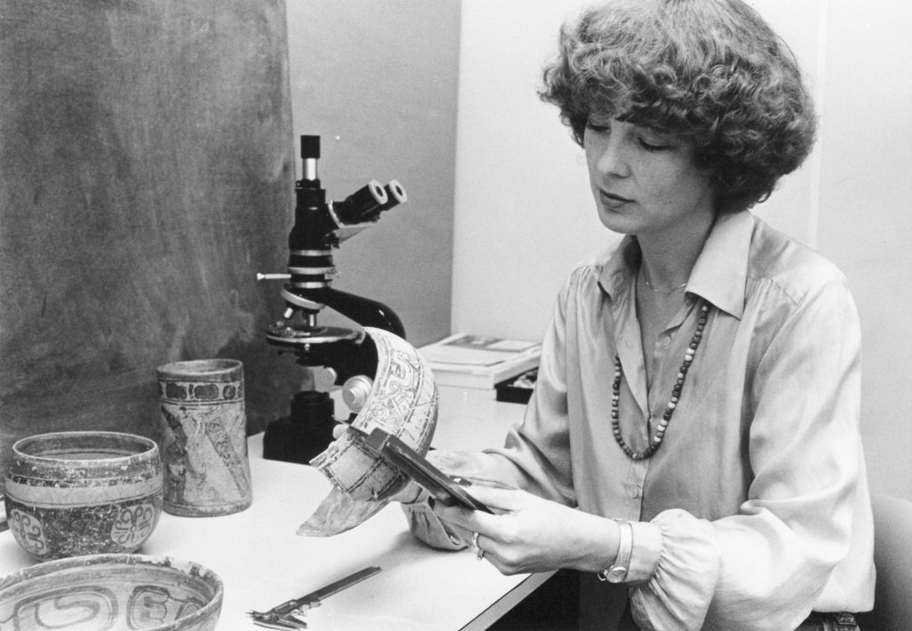 Person inspects a piece of pottery with a measuring device. This is an old, black-and-white photo.