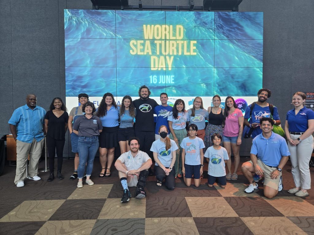 large group of people posing in front of the World Sea Turtle Day sign