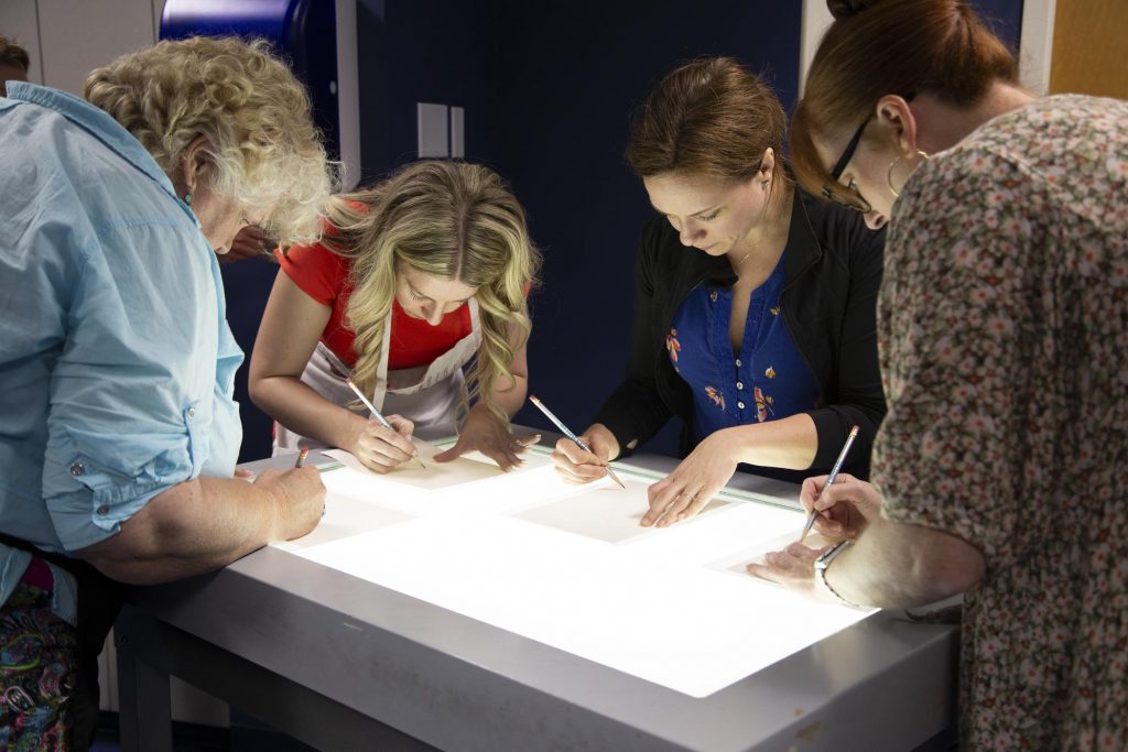 participants use a light table to trace the images they will be painting