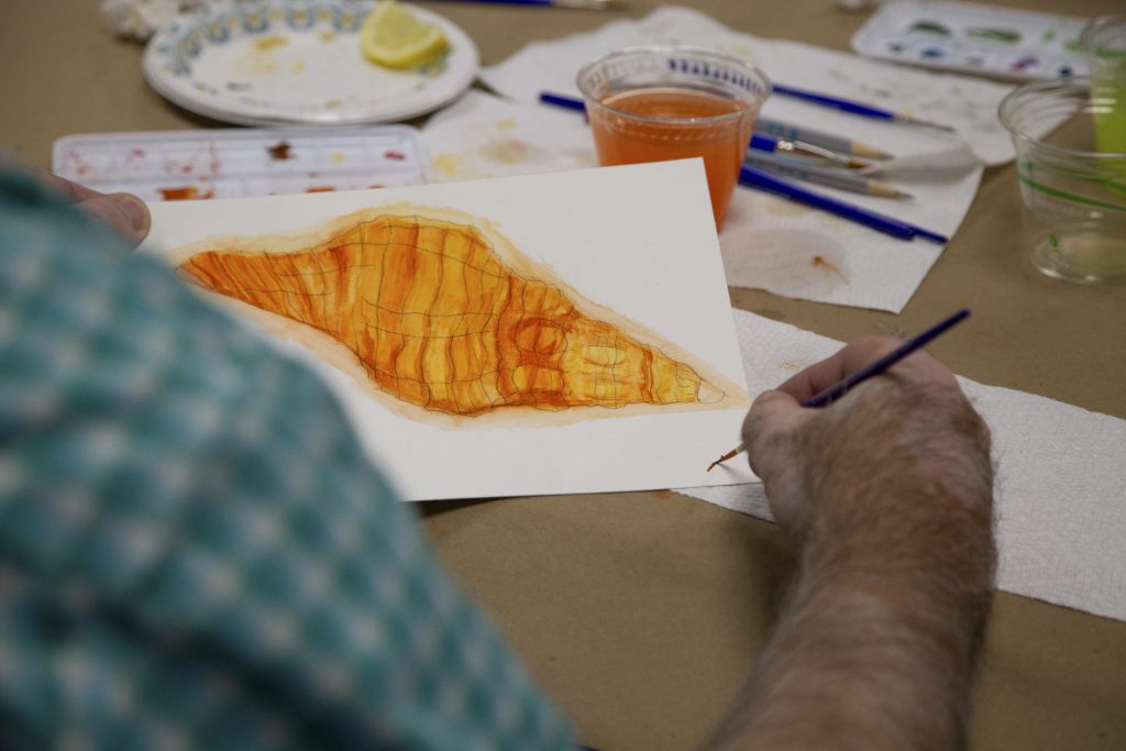 event participant signs his watercolor painting of an orange shell