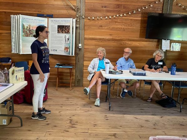 Janelle A. Peña-Jiménez stands as she speaks to a group of volunteers seated at white folding tables.