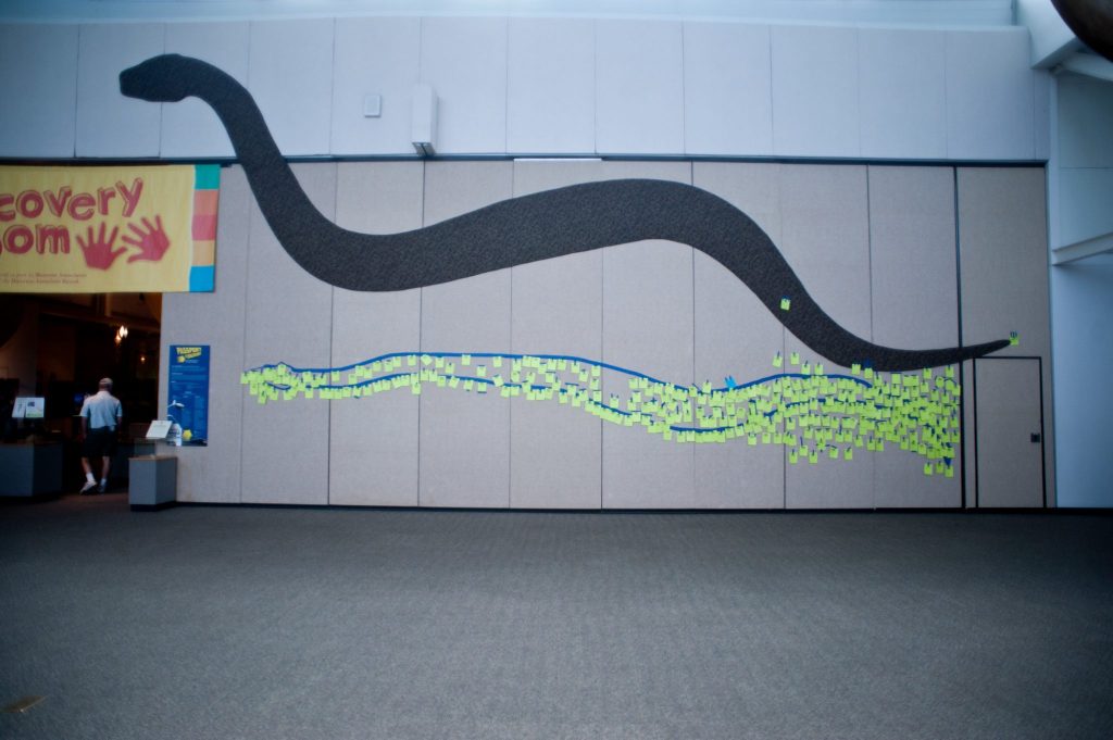 large painted silhouette of titanboa on the wall of the museum, below it are many yellow post-it notes left by museum visitors