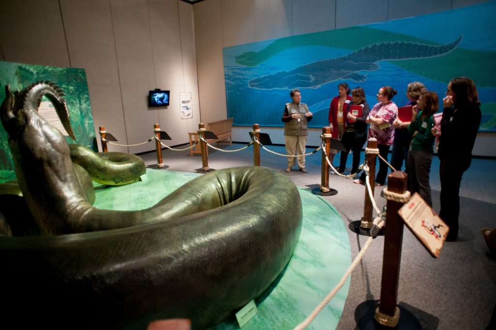 an exhibit guide speaks with a group of visitors in front of the life size model of the titanboa