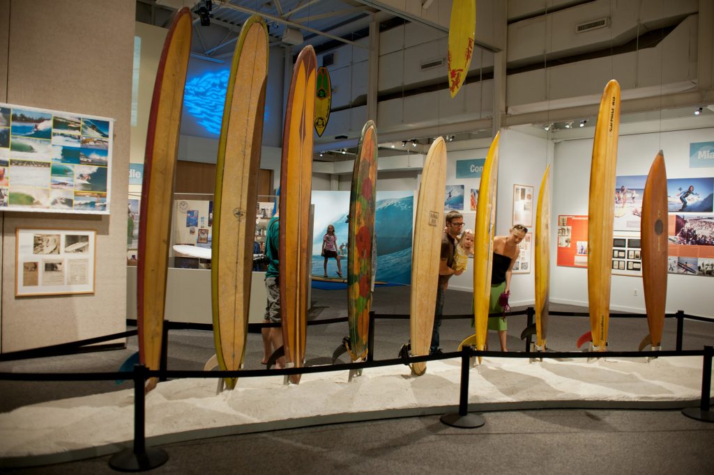 visitors look at a row of tall surfboards