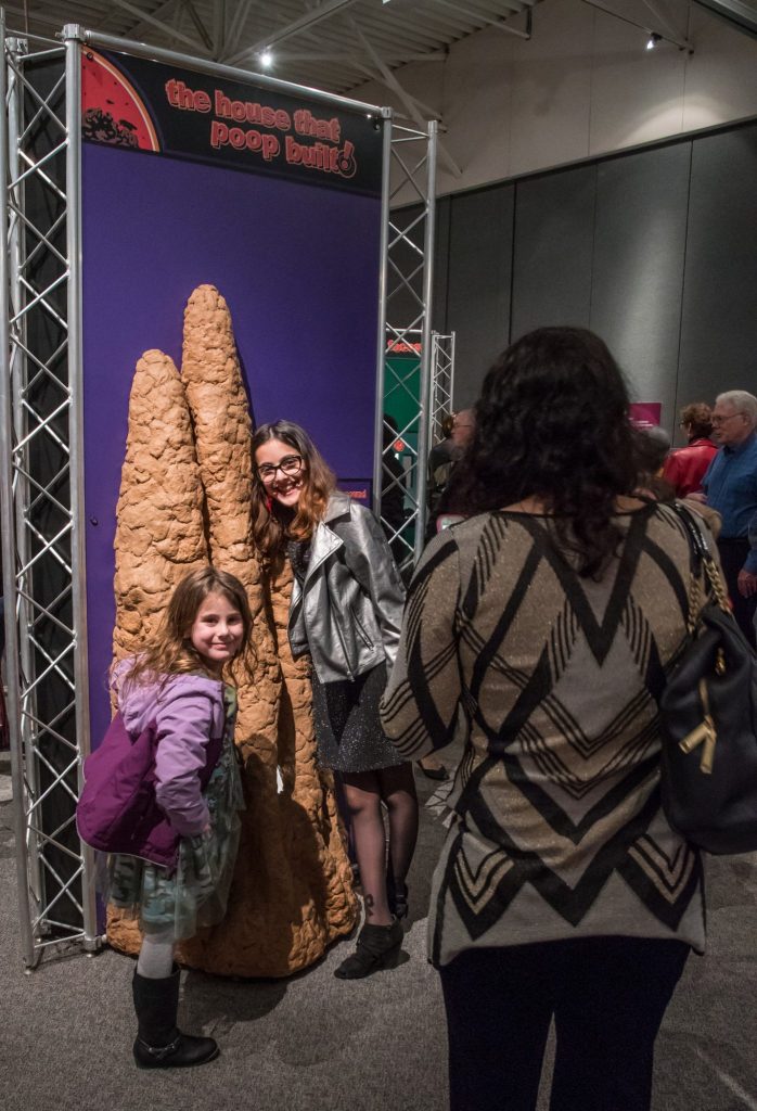 visitors are photographed stand next to large display that reads 'the house that poop built'