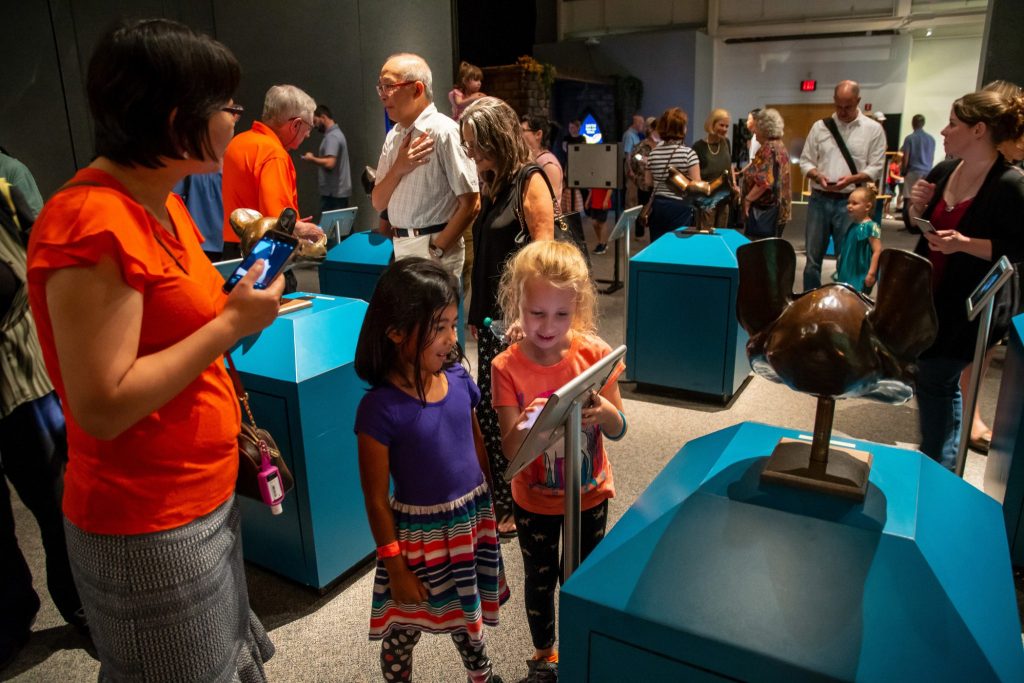 tow young children reading about an item on display, behind them are many people and displays in the bat exhibit