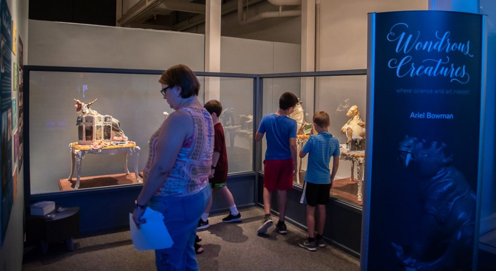 several people looking at the Wondrous Creatures sculptures and reading information displayed on the wall of the exhibit