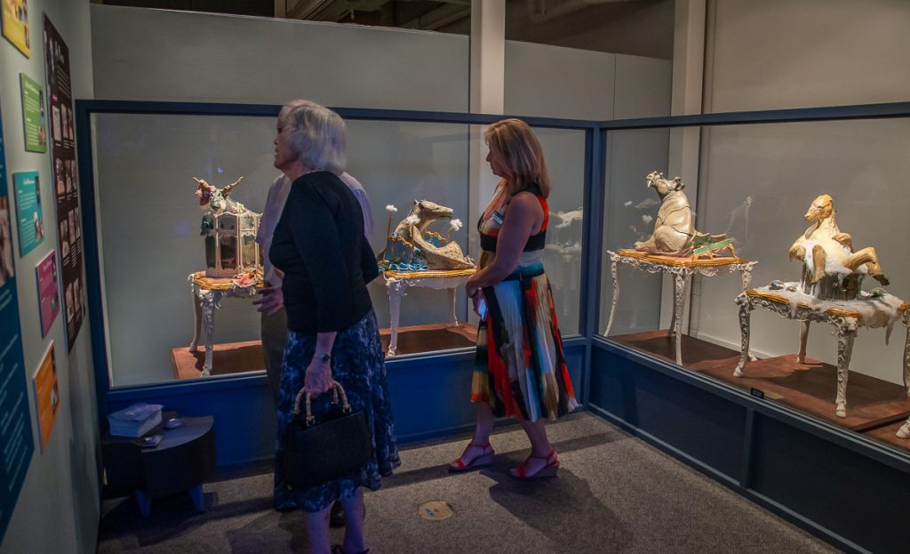 Wondrous creatures exhibit with sculptures behind glass. Several people are looking at the sculptures and reading the information displayed on the wall