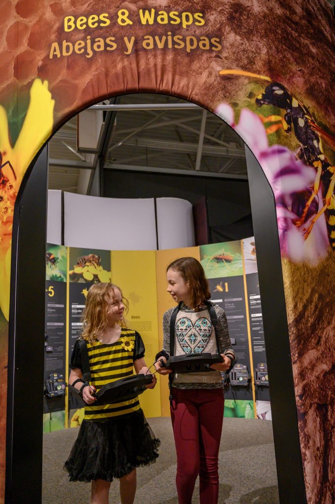two young girls look at each other and smile as the walk through the exhibit