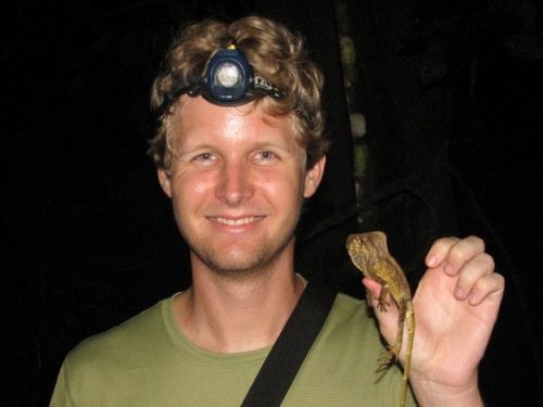 person smiling at the camera he holding a chameleon in one hand