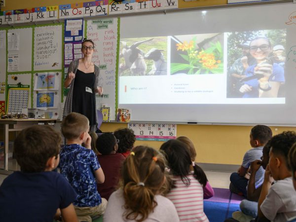 A scientist presents using a Powerpoint to a classroom of students.