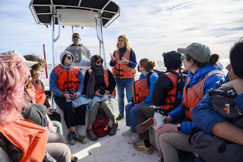 Fellows sitting on the boat looking up at Leslie Sturmer as she stands up and talks about clam leases.