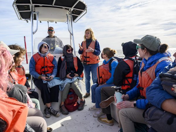 Fellows sitting on the boat looking up at Leslie Sturmer as she stands up and talks about clam leases.