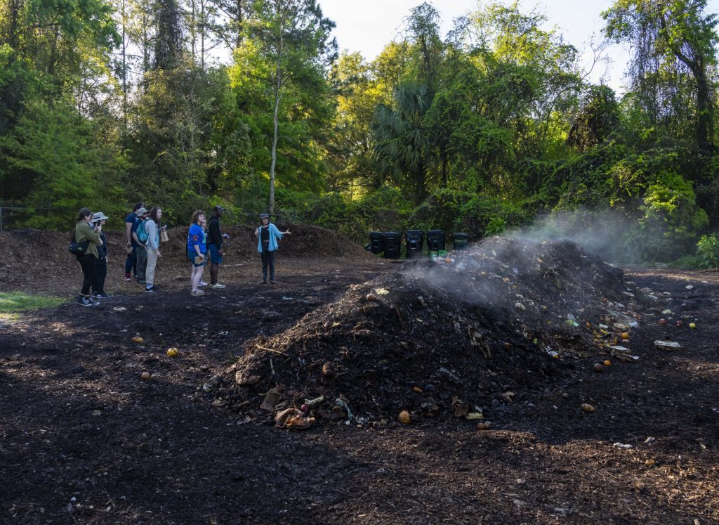 Students stand next to steaming compost pile.