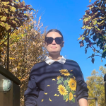 Half body shot of Lexi wearing a navy sweater with sunflowers on it.