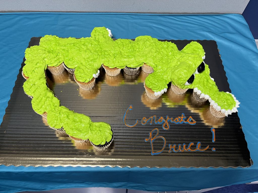 Close up of the cupcake cake of a Florida Gator with bright green frosting. The cardboard the cupcakes sit on says Congrats Bruce in frosting.