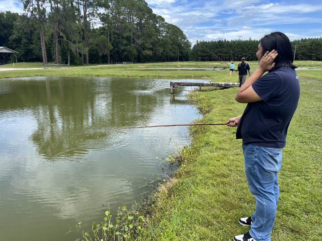 Gregory Nobleza holding a fishing rod over pond water waiting for a fish to take the bait.