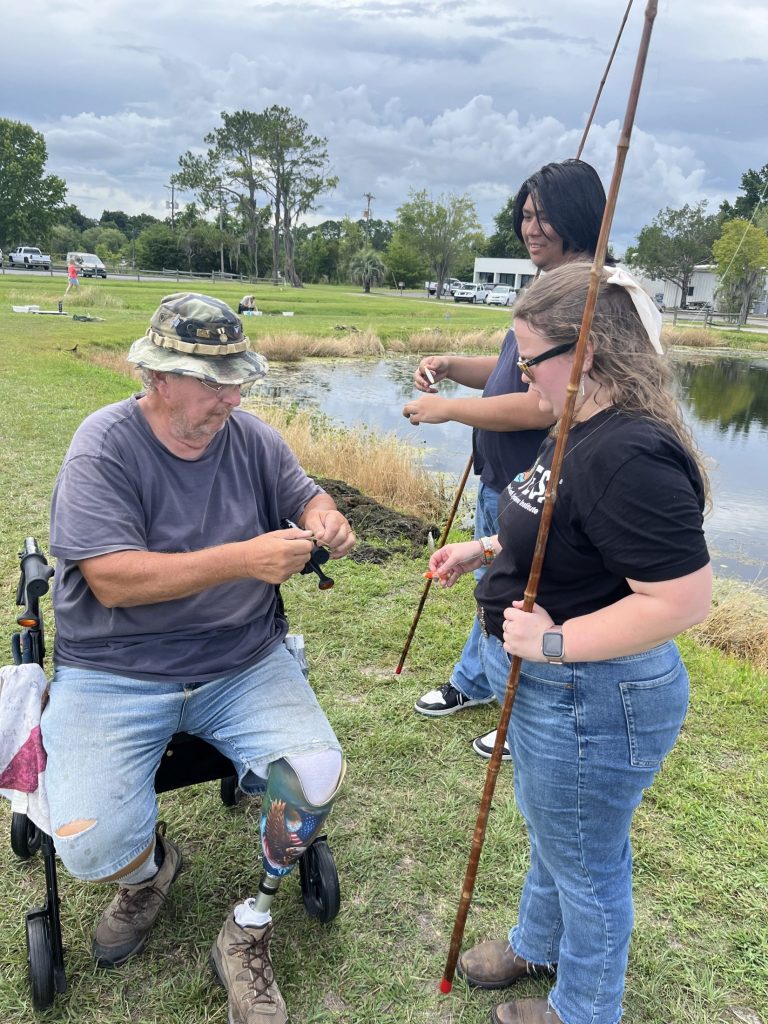 Laura and Gregory talking to a coordinator at Fishing for Success while the coordinator demonstrates something.