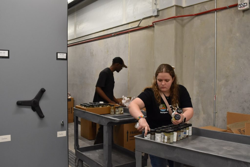 Laura and Joel are separately sorting through fish in jars that are on a rolling cart.