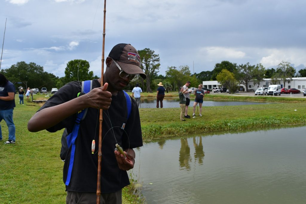 Joel holds the fish he caught from the pond in one hand and examines it.