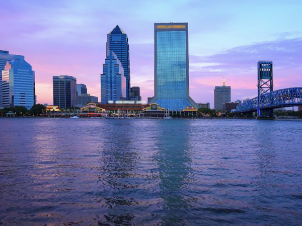 St.Johns river during a purple and pink sky sunset with a skyline of buildings and a bridge to the right.